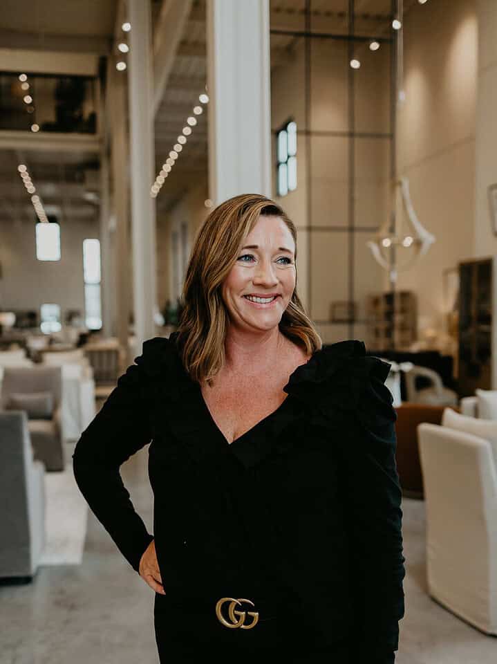 Melissa Froehlich is in a modern, well-lit interior space with high ceilings and minimalist furnishings, smiling and casually posing for the camera.